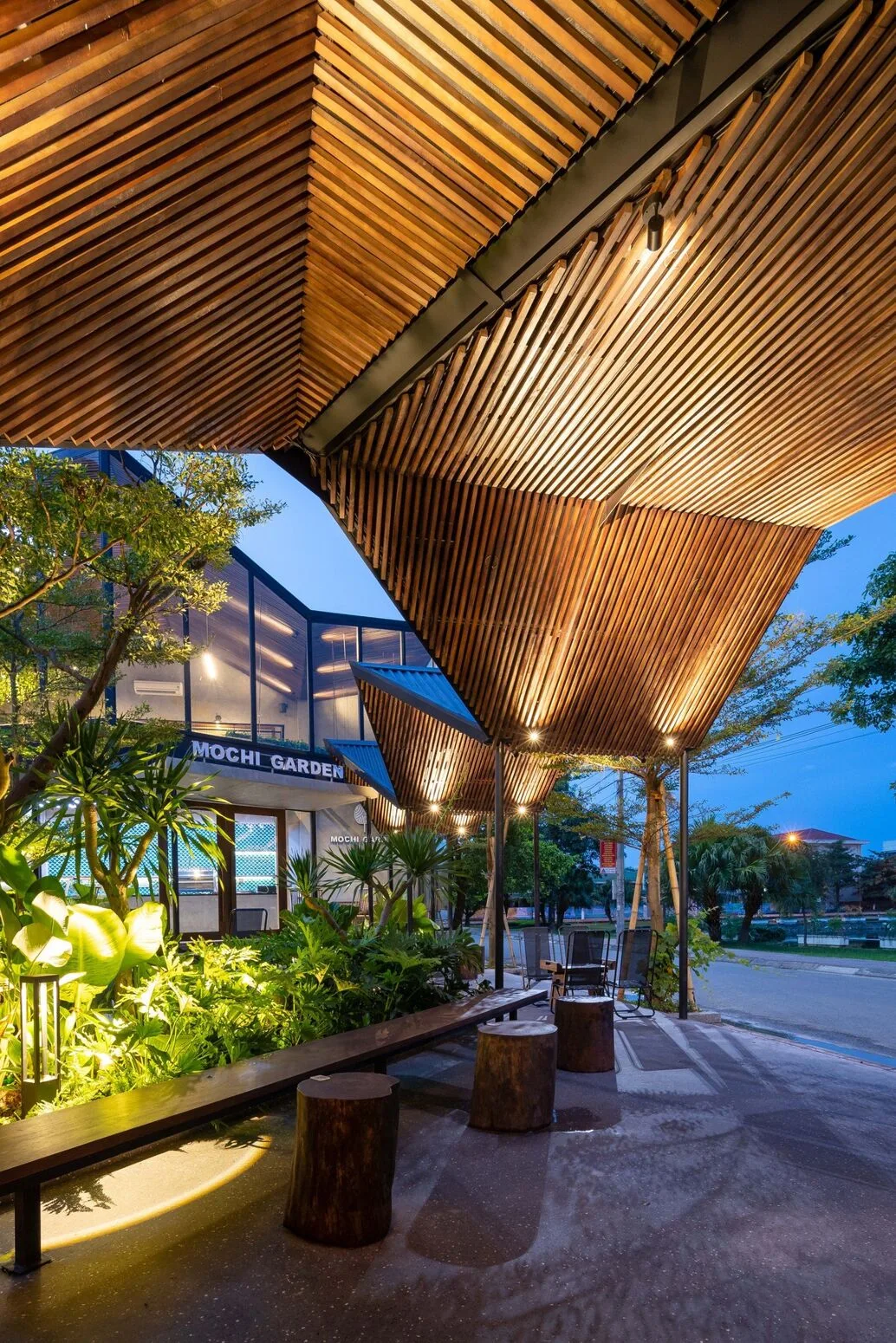 The pavilion roof from below at dusk — light following the timber slats