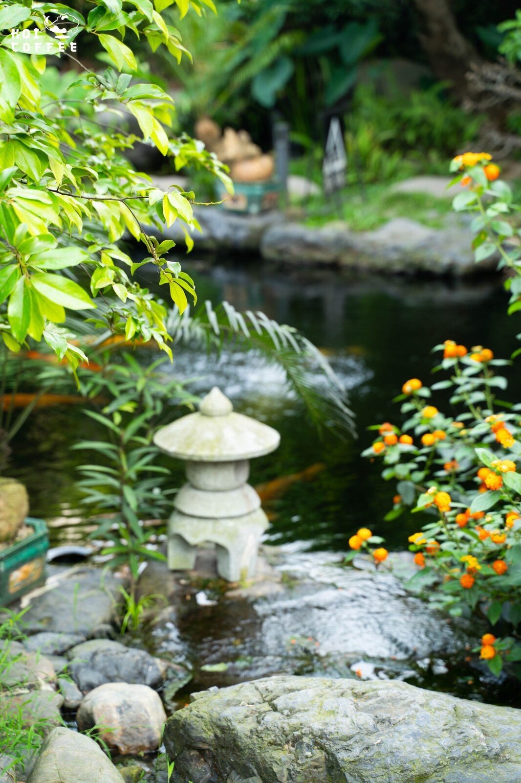 Đèn đá và khóm hoa bên hồ — chi tiết nhỏ, ánh sáng vừa đủ